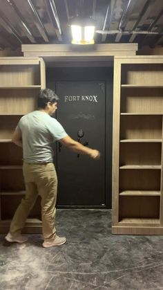 a man standing in front of a tall bookcase with his hand on the door