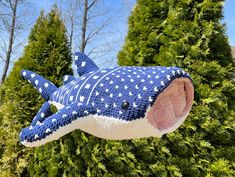 a blue and white knitted shark ornament hanging from a tree with trees in the background