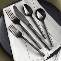 a black plate topped with silverware on top of a white and black table cloth