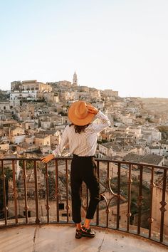 a woman standing on top of a balcony next to a city filled with tall buildings