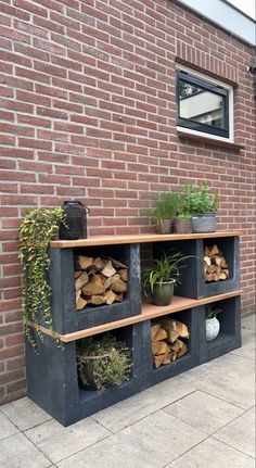 an outdoor firewood rack with potted plants and logs in front of a brick wall