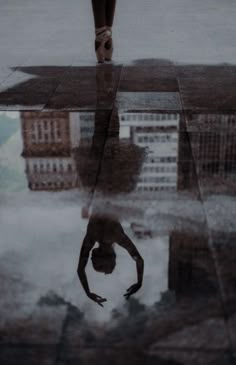 a person standing in the rain with their reflection on the wet ground and buildings behind them