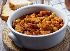 a white bowl filled with stew next to slices of bread on top of a wooden table