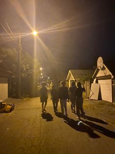 a group of people walking down a street at night with the sun shining on them