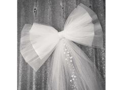 a white tulle bow hanging on the side of a metal wall with sequins