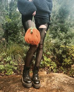 a woman wearing black stockings and holding an orange handbag while sitting on top of a rock