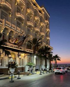 the hotel is lit up at night with palm trees and cars parked on the street