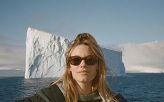 a woman wearing sunglasses standing in front of an iceberg