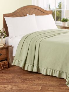 a bed with white sheets and green bedspread next to a wooden headboard