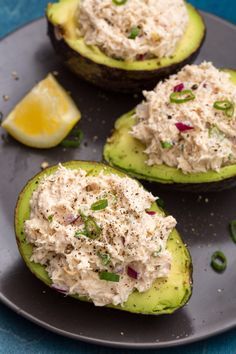 three stuffed avocados topped with tuna salad on a black plate next to a lemon wedge