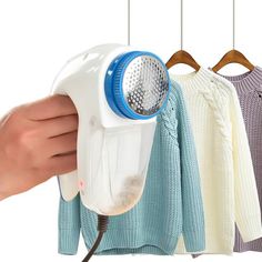 a person holding an electric hair dryer in front of three sweaters