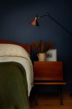 a bedroom with a bed, night stand and plant on the nightstand next to it