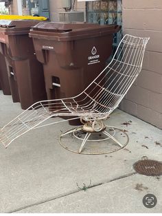 a metal chair sitting on top of a sidewalk next to trash cans and bins