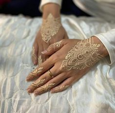 two hands with henna tattoos on them sitting on a bed next to each other