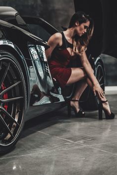 a woman leaning on the side of a black sports car with her foot in the door