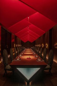 a long table with chairs and plates on it in a room that has red lighting