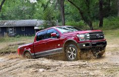 a red truck is driving through the mud in front of some trees and a barn