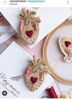 two heart brooches sitting on top of a table next to some sewing needles