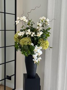 a black vase filled with white and green flowers