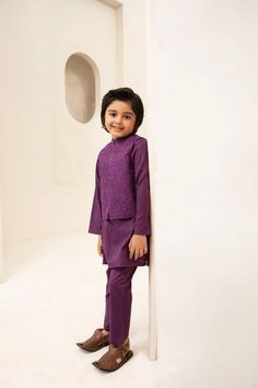 a little boy in a purple suit standing next to a white wall