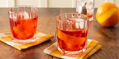 two glasses filled with liquid sitting on top of a wooden table next to an orange