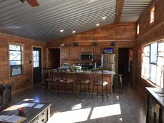 a kitchen and living room with wood paneling on the walls, ceiling fan and windows