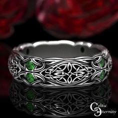 a wedding band with green stones in the center and celtic designs on it's sides