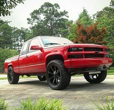 the red truck is parked in front of some trees and bushes with black rims