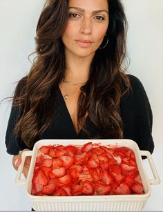 a woman holding a white dish full of strawberries