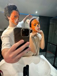 two people with orange face paint on their faces taking a selfie in front of a mirror