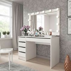 a white vanity with lights on it and flowers in vases next to the mirror