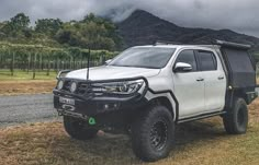 a white truck parked on the side of a road next to a field with mountains in the background