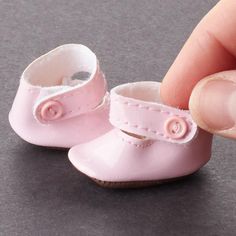 a small pink baby bootie is being held by a person's finger on a gray surface