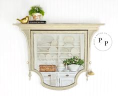 an old china cabinet with plates and plants on top is displayed against a white wall