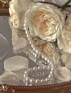 white roses and pearls are sitting on a glass table with a mirror behind it that is reflecting water