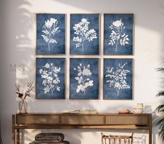 four blue and white floral prints on a wall above a console table with wicker chairs