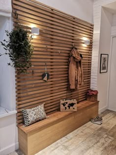 a wooden bench sitting in front of a wall with coat hanging on it's side