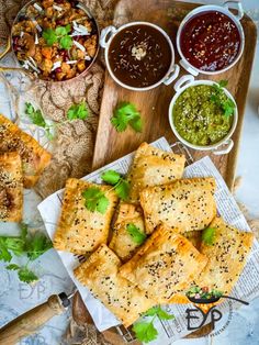 several different types of food are on a wooden platter with dipping sauces and condiments