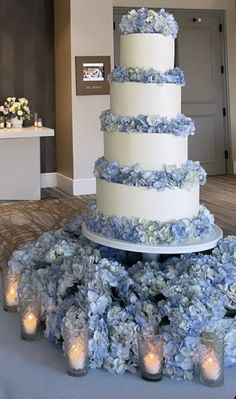 a white and blue wedding cake surrounded by candles on a table in a room with flowers