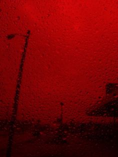 rain drops on the windshield of a car as it drives down a street in front of a red light