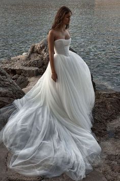 a woman in a white dress standing on rocks near the water with her hands behind her back