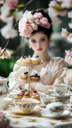 a woman with flowers in her hair is sitting at a table with tea and pastries