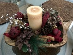 a candle sits on top of a wooden bowl filled with pine cones and other decorations