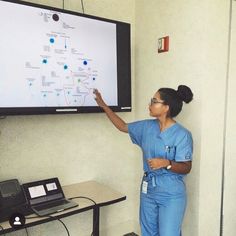 a woman in scrubs points at a whiteboard