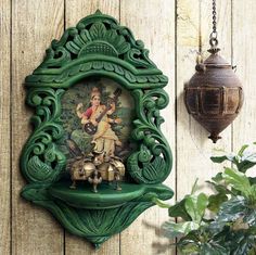 an ornate green frame hangs on the wall next to a potted plant and lamp