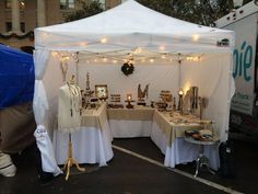 a tent with tables covered in white cloths and lights hanging from it's sides