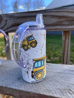 a glass cup with a yellow construction truck design on it sitting on a wooden bench