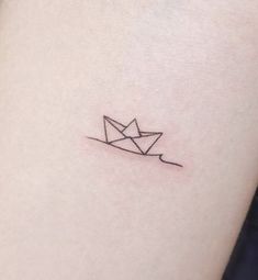 a small origami paper boat tattoo on the right side of the left arm