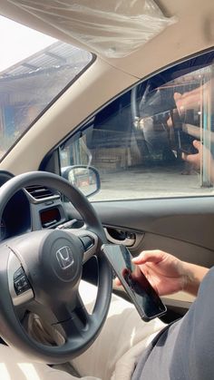 a person sitting in a car using a cell phone while holding an electronic device with both hands