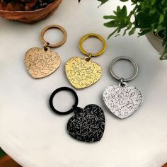 four different styles of heart shaped key chains on a table next to a potted plant